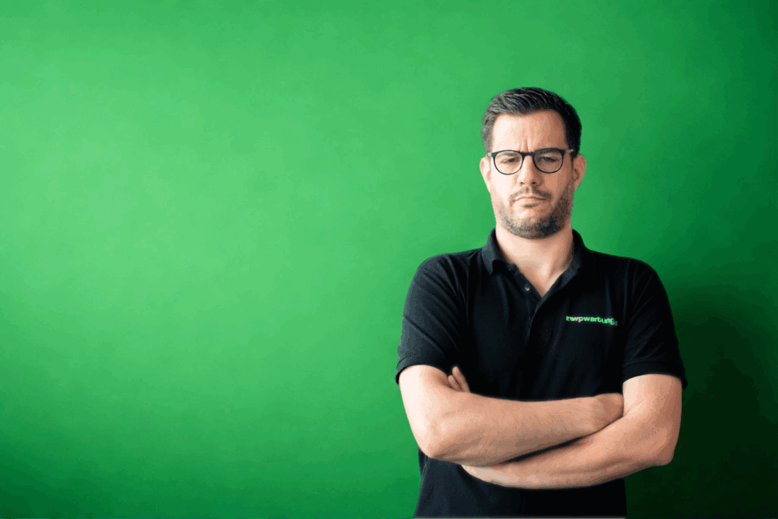 Mann mit verschränkten Armen und skeptischem Blick, grüner Hintergrund