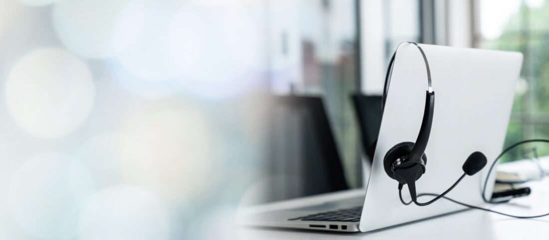 Headset mit Mikrofon hängt an einem Laptop, im Hintergrund unscharfes Büro